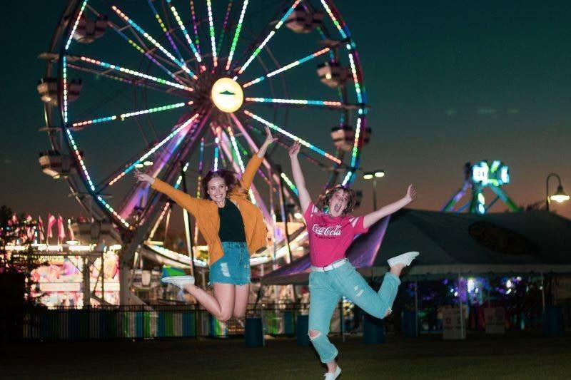 Friends jumping for joy in front of a lit ferris wheel at a night carnival